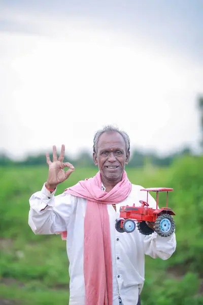 stock image Indian farmer holding mini tractor toy for loan and banking , success of poor and old farmer