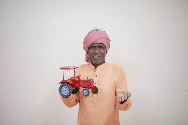 stock image Indian farmer holding mini tractor toy for loan and banking , success of poor and old farmer