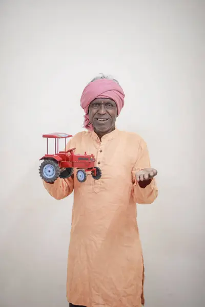 stock image Indian farmer holding mini tractor toy for loan and banking , success of poor and old farmer