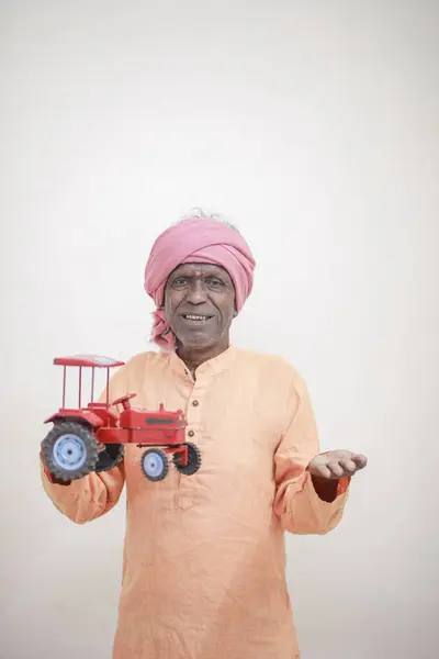 stock image Indian farmer holding mini tractor toy for loan and banking , success of poor and old farmer