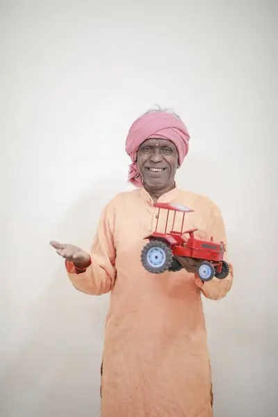 stock image Indian farmer holding mini tractor toy for loan and banking , success of poor and old farmer