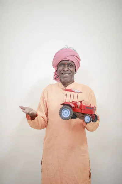 stock image Indian farmer holding mini tractor toy for loan and banking , success of poor and old farmer