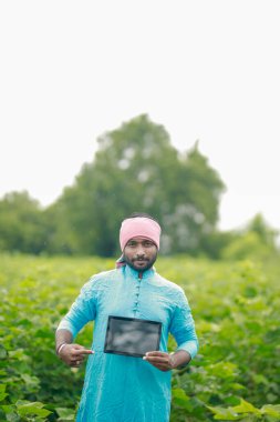 Mutlu genç Hintli çiftçi akıllı telefon kullanıyor, çiftçi tablet gösteriyor, ekranı işaret ediyor