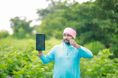 Mutlu genç Hintli çiftçi akıllı telefon kullanıyor, çiftçi tablet gösteriyor, ekranı işaret ediyor