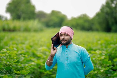 Mutlu genç Hintli çiftçi akıllı telefon kullanıyor, çiftçi tablet gösteriyor, ekranı işaret ediyor