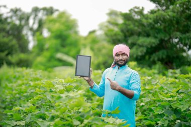 Mutlu genç Hintli çiftçi akıllı telefon kullanıyor, çiftçi tablet gösteriyor, ekranı işaret ediyor