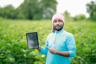 Mutlu genç Hintli çiftçi akıllı telefon kullanıyor, çiftçi tablet gösteriyor, ekranı işaret ediyor