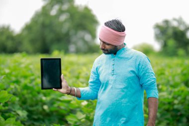 Mutlu genç Hintli çiftçi akıllı telefon kullanıyor, çiftçi tablet gösteriyor, ekranı işaret ediyor