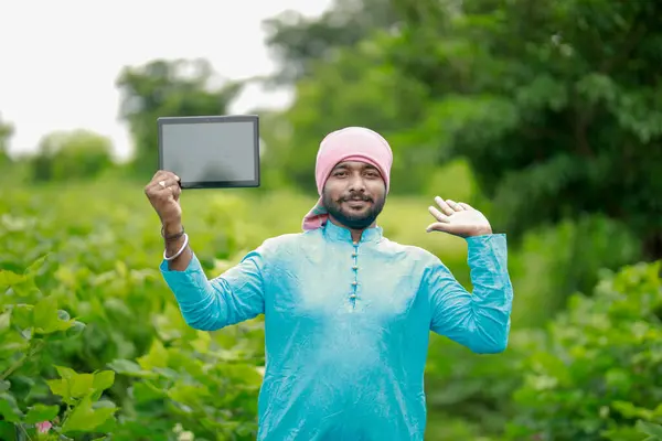 Mutlu genç Hintli çiftçi akıllı telefon kullanıyor, çiftçi tablet gösteriyor, ekranı işaret ediyor