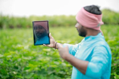 Mutlu genç Hintli çiftçi akıllı telefon kullanıyor, çiftçi tablet gösteriyor, ekranı işaret ediyor