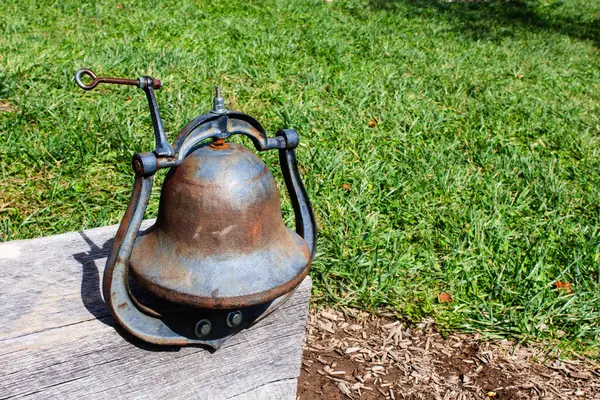 Antique metal bell on a wooden table in the garden with green grass