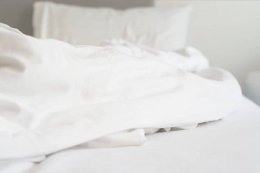 Yatak odasındaki kırışık, dağınık battaniye ve beyaz yastık sabah uyandıktan sonra, uzun bir gece uyuduktan sonra, yorgan ve battaniyenin ayrıntıları, otel odasında beyaz battaniyeli yapılmamış bir yatak..