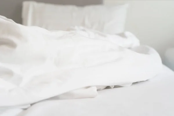 wrinkle messy blanket and white pillow in bedroom after waking up in the morning, from sleeping in a long night, details of duvet and blanket, an unmade bed in hotel bedroom with white blanket.