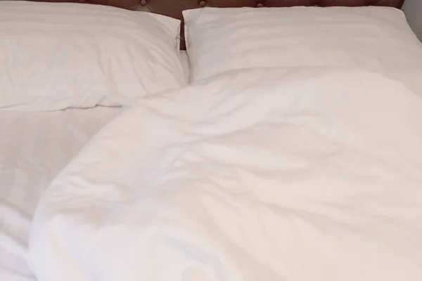 white pillows and white sheets on messy bed after waking up in the morning.
