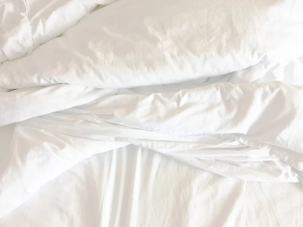 White pillow on bed and with wrinkle messy blanket in bedroom.