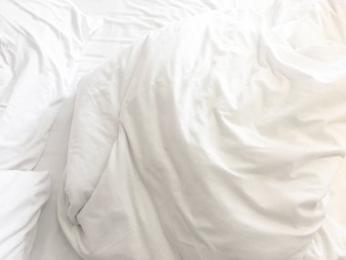 Yatak odasındaki kırışık, dağınık battaniye ve beyaz yastık sabah uyandıktan sonra, uzun bir gece uyuduktan sonra, yorgan ve battaniyenin ayrıntıları, otel odasında beyaz battaniyeli yapılmamış bir yatak..