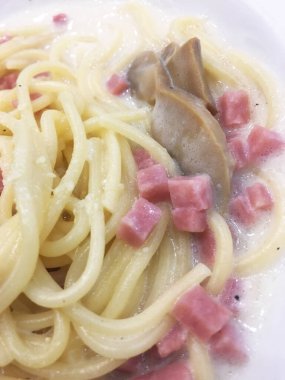 Jambon ve mısırla karıştırılmış beyaz krema soslu spagetti ve beyaz bir tabakta servis ediliyor. .
