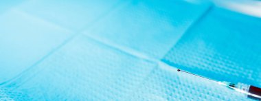 Şırınganın ucunda bir damla kan olan şırınganın yakın çekimi tıbbi tepsinin üzerinde tutuluyor.