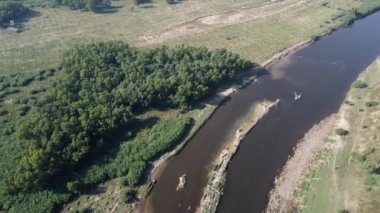 Vahşi yaşam açısından zengin, yemyeşil bir ormanda kıvrılan çamurlu bir nehrin havadan görünüşünü hayal edin. Bu çarpıcı manzara doğa ve tarım arasındaki uyumu vurguluyor.,