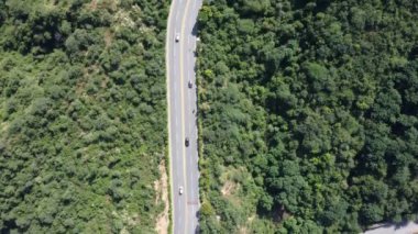 İnsansız hava aracı, dolambaçlı bir yolun yoğun yeşillik boyunca zarafetle kıvrıldığı verimli bir ormanı yakalar. Araçlar dar yolda ilerler, doğayı trafiğin ritmiyle harmanlarlar..