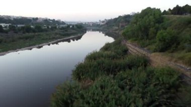 İnsansız hava aracı Kuğu Nehri 'nin bulanık sularından ayrılır. Çevredeki manzarayı ve yerleşim yerlerini ortaya çıkarır..