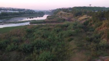 Günbatımında dron, su atığının bulanık sularla karıştığı Kuğu Nehri 'ni yakalar ve canlı gökyüzünün yüzeye yansımasıyla kirliliği etkiler..