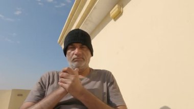 Siyah şapkalı bir adam yüzünü gösteriyor ki bu ona hiç yakışmıyor ellerini ovuşturuyor.