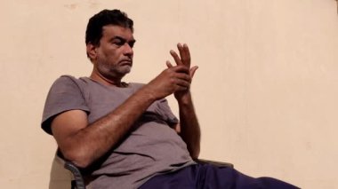 Bir adam güneşte oturuyor, bir şey düşünüyor ve ellerine bakıyor, hayal kırıklığını ifade ediyor..