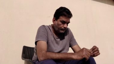 Zavallı adam güneşli bir günde dışarıda oturmuş stres içinde başını sağa sola sallıyor ve umutsuz görünüyor.