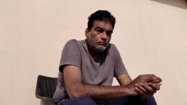 Gergin bir şekilde dışarıda oturan gergin bir adam bazen aşağıya bakar ve iki elini de birbirine sürter.