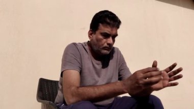 Orta yaşlı bir adam iki eliyle oynuyor ve güneşli bir günde dışarıda otururken bir şeyler düşünüyor.