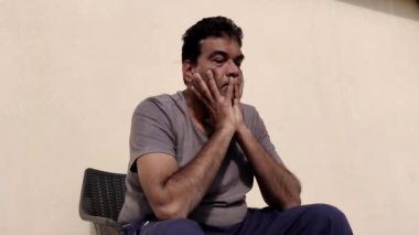 Güneşli bir günde, dışarıda oturan zavallı bir adam iki eliyle yüzünü ovuşturuyor. Dışarıdaki huzurlu ortamın aksine endişe duyuyor. Gün ışığında bir anlık stres ve yansıma.