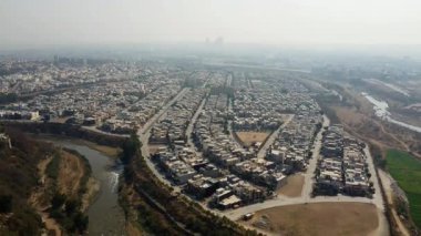 Gayri menkul 4K Hava Aracı Parlak Güneşli bir günde Nehir ve Tarım Arazisi ile çevrili bir şehrin görüntüsü
