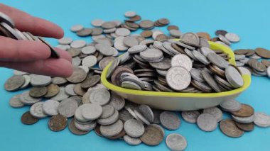 Disiplinli birikimleri ve servet biriktirmenin ödüllü yolculuğunu temsil eden açık mavi arka planda büyüyen yığına madeni paralar ekliyor. Metalik paralar, finansal hedefleri ve başarıyı simgeleyen sakin bir zemin ile tezat oluşturuyor.