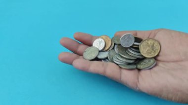 Bir avuç dolusu bozuk para, tepesinden aşağı düşer. Bu, Ramazan ayındaki zekat talebini simgeler. Açık mavi arka plan ve metalik madeni paralar kutsal ayda İslami yardım, inanç ve sosyal sorumluluk temalarını çağrıştırıyor.