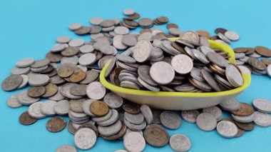 Bir kaseye düşen çeşitli madeni paralar açık mavi arka plandaki finansal büyümeyi sembolize eder