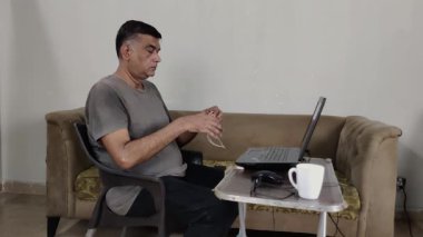 Adam kulaklıkları bilgisayara takarken ve bardakları yerleştirirken belirsiz görünüyor.