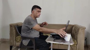 Evden çalışan adam çay molasından sonra dizüstü bilgisayarına devam eder ve gözlüğünü alır.