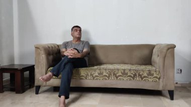 Endişeli adam etrafa bakar ve yalnız başına koltukta otururken zihinsel yorgunluğu ve stresi yansıtır.