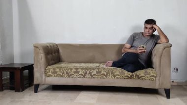 Zihinsel olarak boşaltılmış adam telefonu bir anda kanepeye kaydırırken kafasının üstünde dinleniyor.