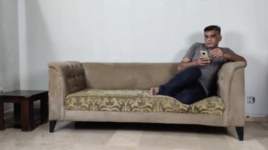 Adam elinde cep telefonu olan ve rahatsız edici veya derin dijital emilimi olan garip bir pozisyonda oturuyor