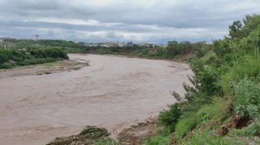 Nüfusun yoğun olduğu bölgedeki bulutlu gökyüzünün altında nehir kanalında sürekli akan çamurlu sel suları.