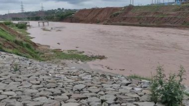 Kahverengi fırtına suyu nehirde yavaşça akıyor. Elektrik hattı bulutlu havada merkezden geçiyor.
