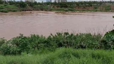 Bulutlu bir günde şehirde araçlar geçerken düşük hızda çamurlu su nehirden akar.
