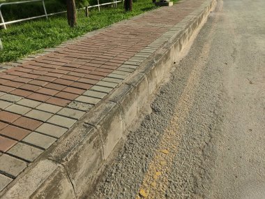 Kırmızı ve bronzlaşmış tuğla kaldırımlar ve asfalt yol arasında gün ışığında açıkta duran beton kaldırım.