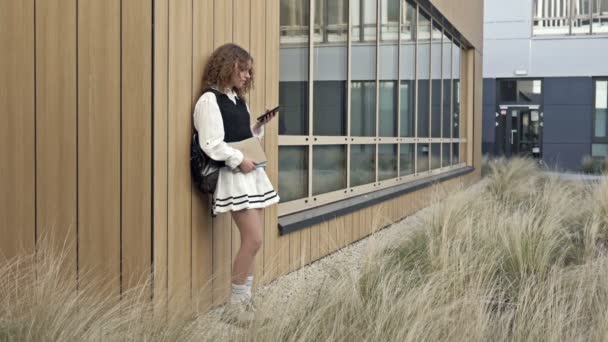 Elinde Telefon Olan Bir Lise Öğrencisi Üniversite Bahçesinde Bir Duvara — Stok video