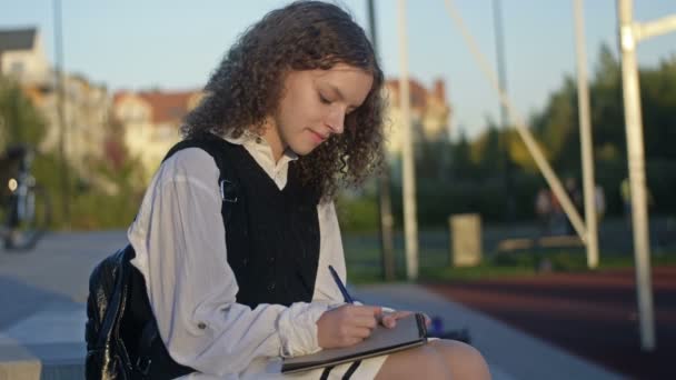 Söpö Koulutyttö Univormussa Kirjoittaa Jotain Muistikirjaan Hän Istuu Yksin Koulun — kuvapankkivideo