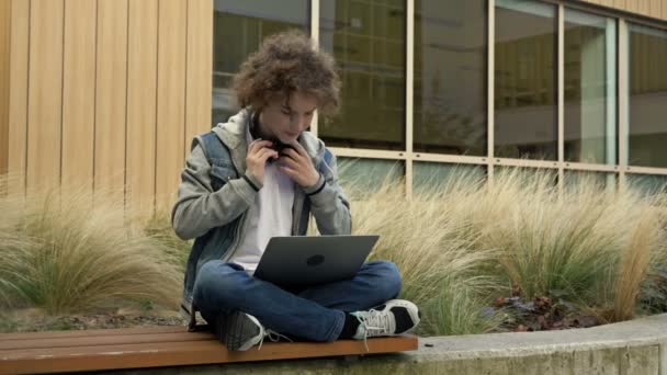 Jóképű Fickó Laptoppal Fejhallgatóval Beszélget Valakivel Gépel Egyszerre — Stock videók
