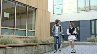 İki sevimli lise öğrencisi, bir erkek ve bir kız, eğitim kurumunun avlusunda dolaşıyorlar. Gençler hareketli konuşuyorlar. 4K.