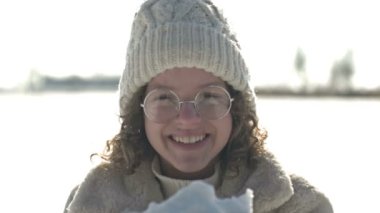 Beyaz örgü şapkalı neşeli genç kız avuçlarından kar üflüyor. HD.